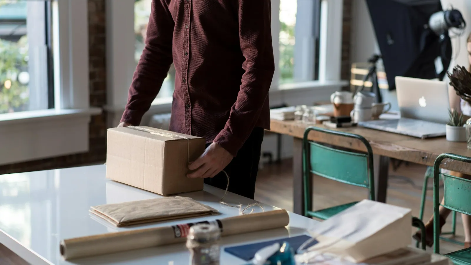 Online store owner holding a packed order box beside a laptop