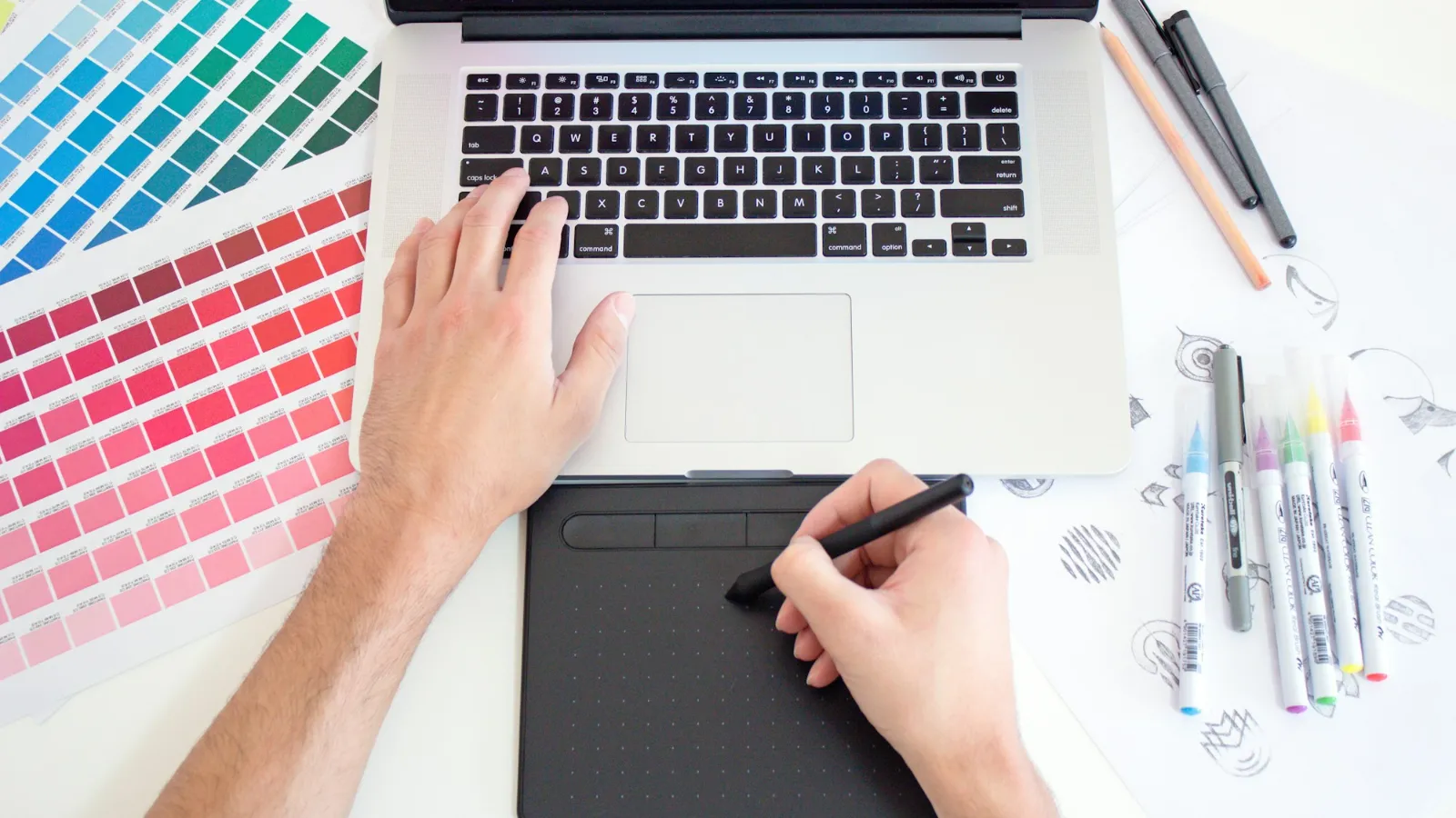 Web designer working on a website layout with a laptop, drawing tablet and colour swatches